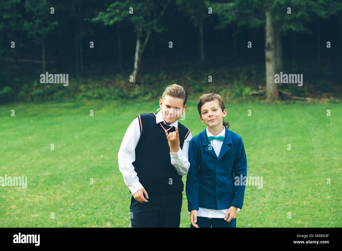 Due ragazzi, fratelli, amici travestiti in abbigliamento formale fare divertimento di fronte a una foresta in un prato in estate. Foto Stock