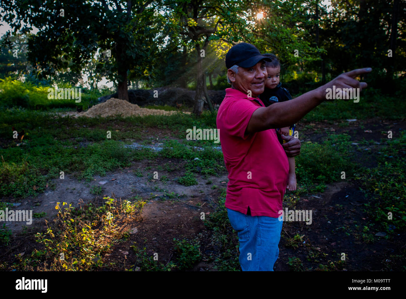 Miguel Ventura, un vescovo salvadoregno indaco naturale produttore, porta un bambino mentre si cammina nelle prime ore del mattino nella sua fattoria vicino a San Miguel, El Salvador. Foto Stock