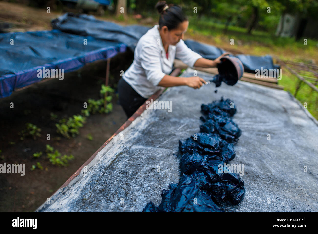 Lavoratore agricolo si diffonde la indigo pasta su un foglio di metallo tabella ad asciugare al sole in fabbricazione vicino a San Miguel, El Salvador. Foto Stock