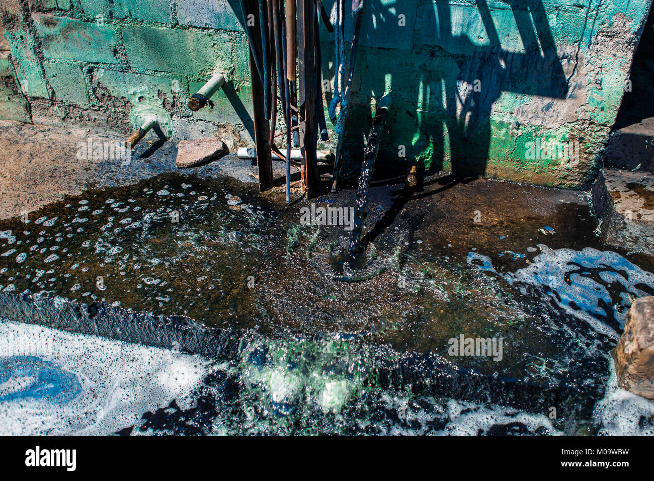 Un blu verdastro la soluzione di acqua è visto sifonato fuori da una cisterna di cemento a semi-fabbricazione industriale vicino a San Miguel, El Salvador. Foto Stock
