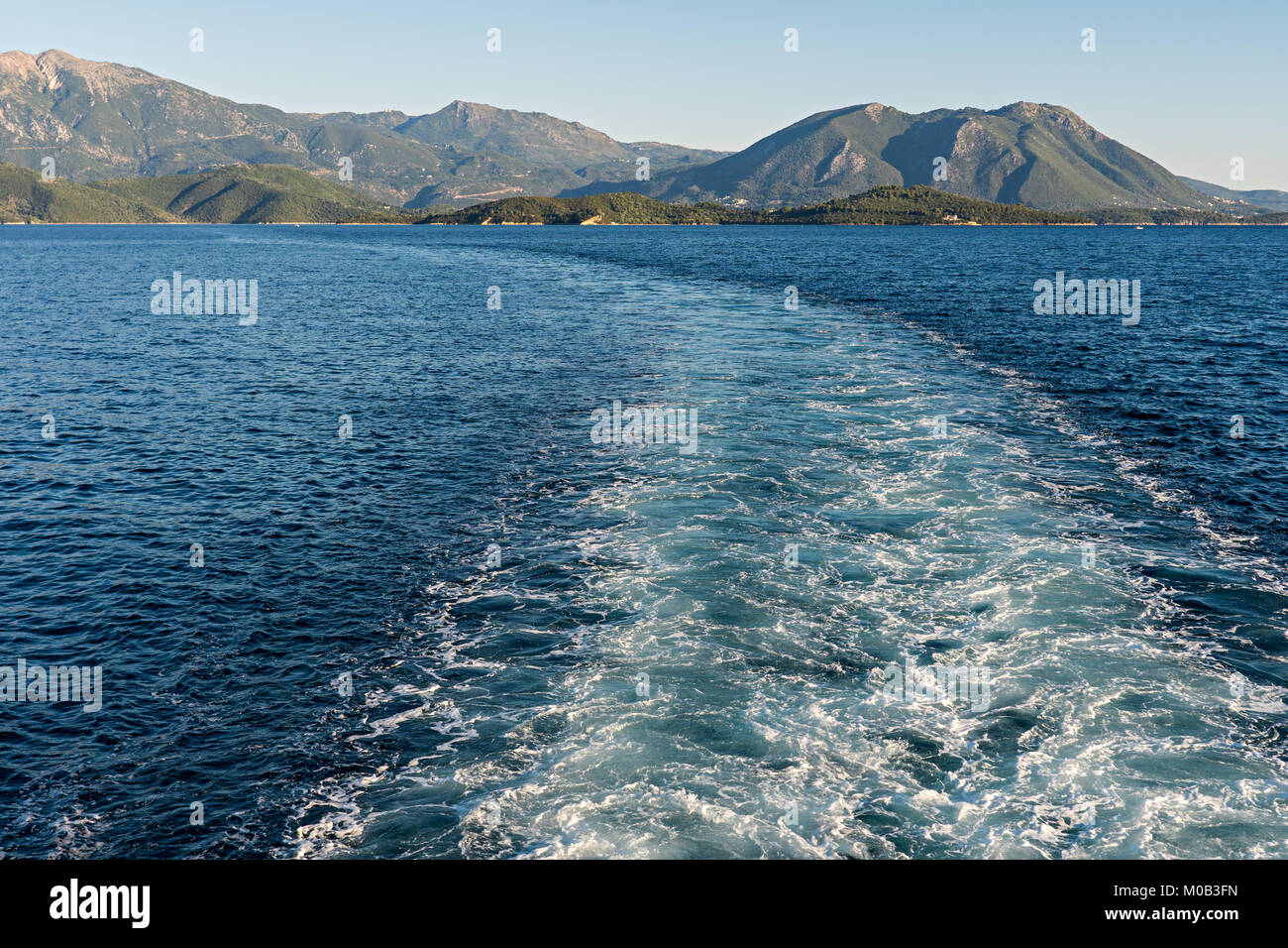 Sentiero sulla superficie del mare dietro una nave con le montagne in distanza Foto Stock