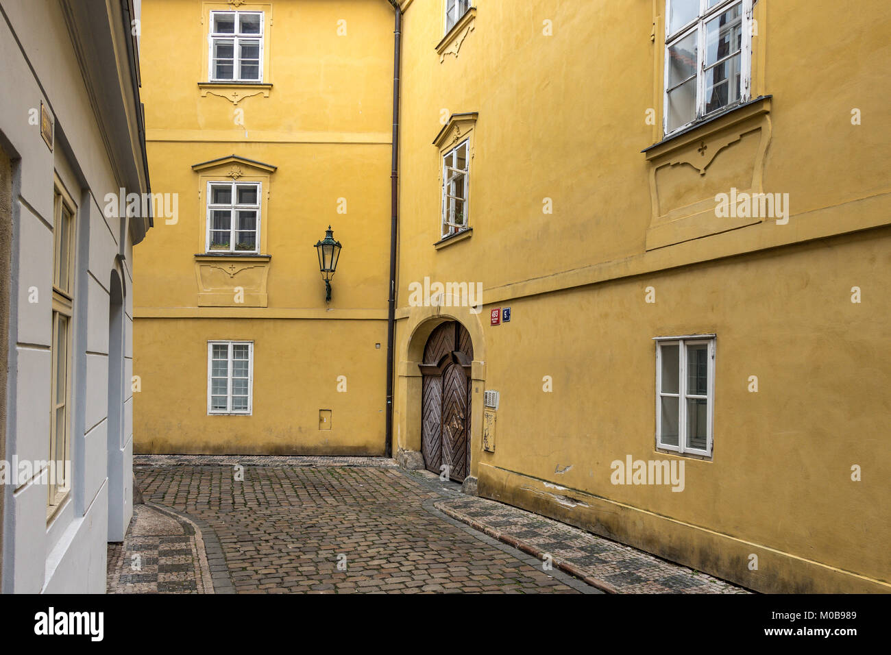 Verniciato giallo edificio con una grande in legno marrone set di gate in un arco , lungo una strada acciottolata a Praga , Repubblica Ceca Foto Stock