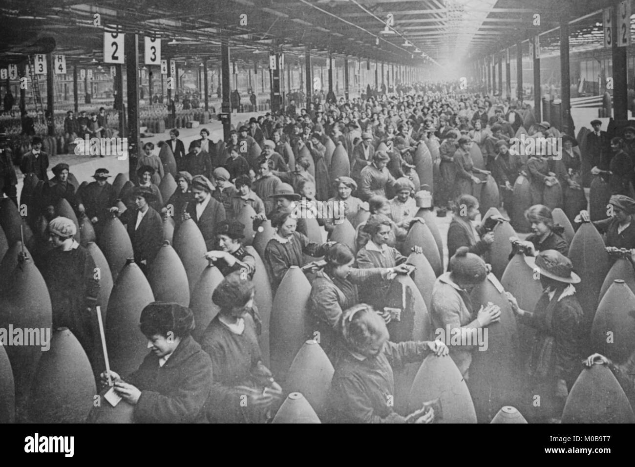 Schiere di donne intercalate fra grandi serbatoi di artiglieria in una fabbrica. Foto Stock
