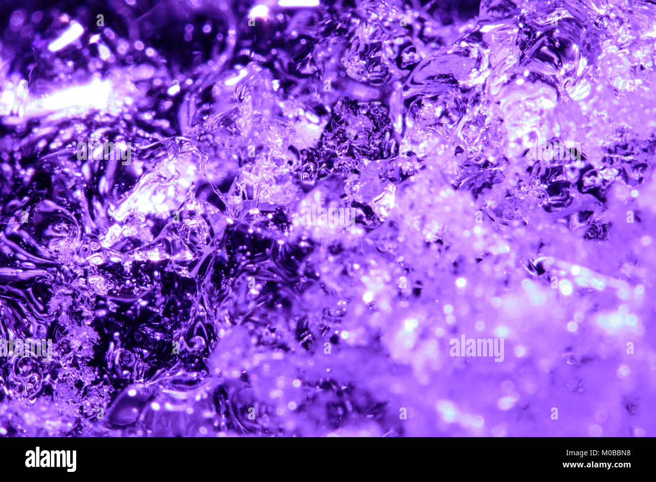 Un pezzo di ghiaccio viola con bolle congelate nell'acqua. Un piccolo iceberg in acqua Foto Stock