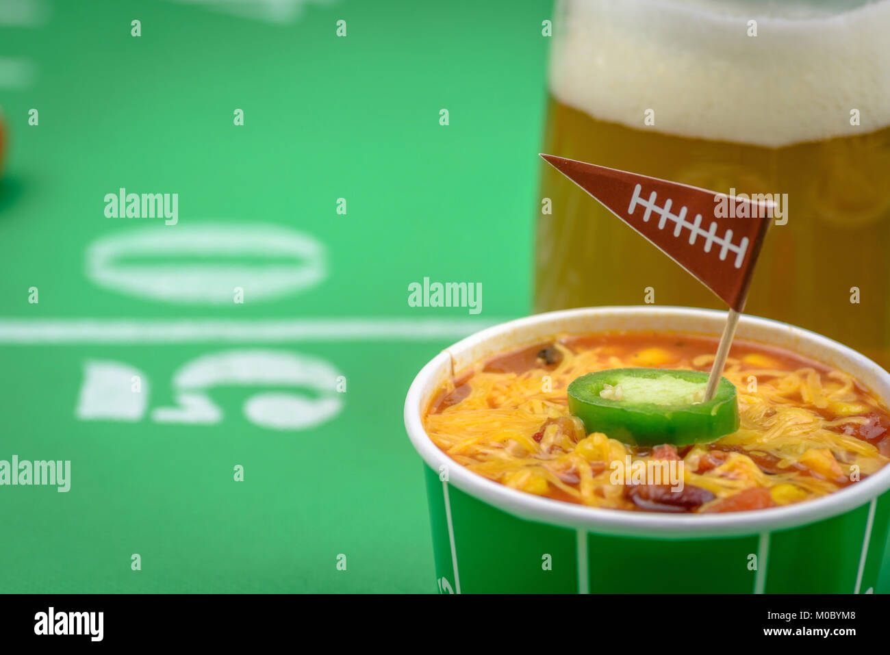 Macro closeup di una piccola ciotola di peperoncino e boccale di birra sul tavolo decorato per il grande gioco di calcio Foto Stock