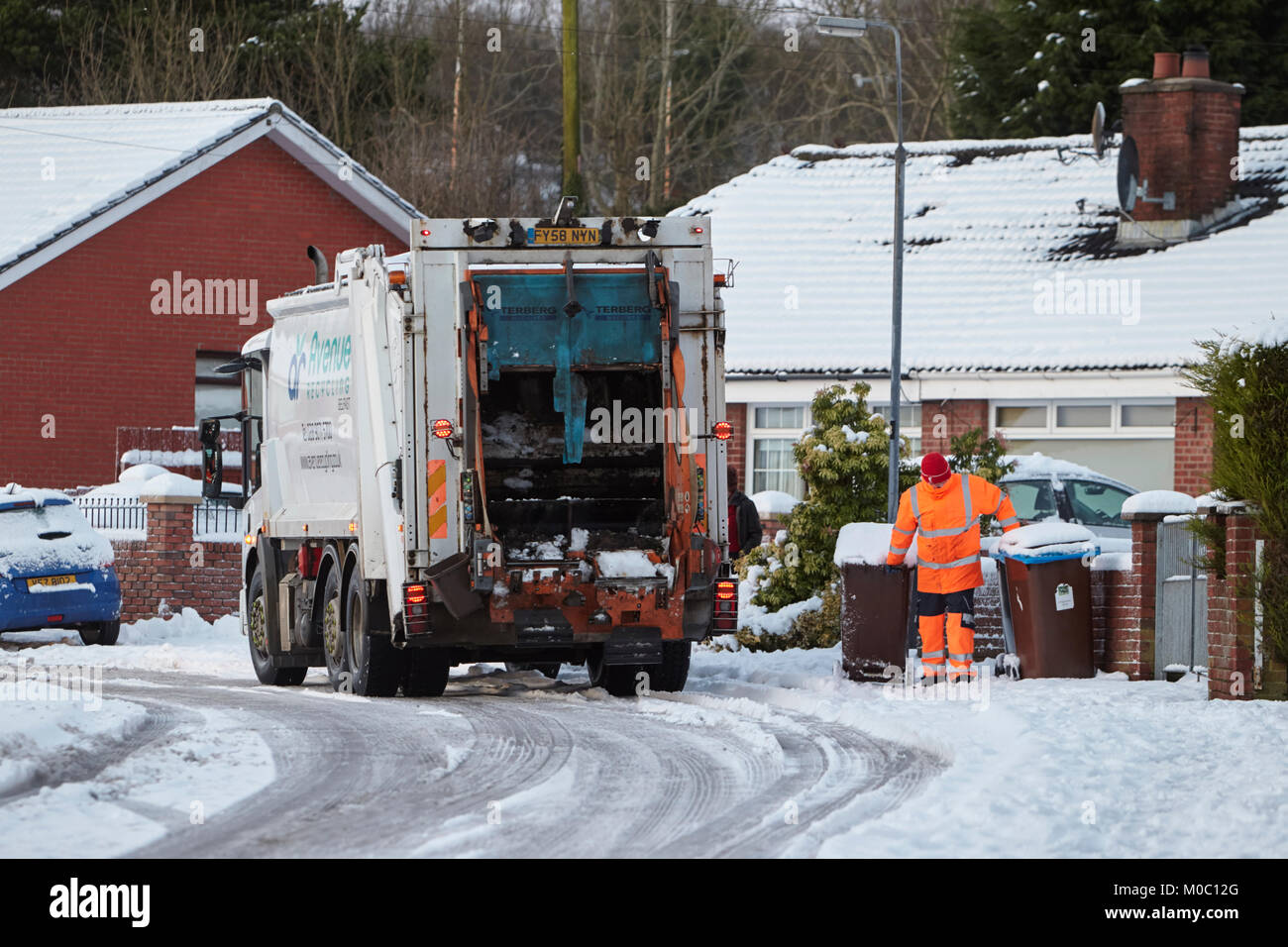 Lavoratore cassonetti di raccolta con il riciclaggio di rifiuti di raccolta di guida del carrello lungo la strada coperta di neve a Newtownabbey Irlanda del Nord Foto Stock