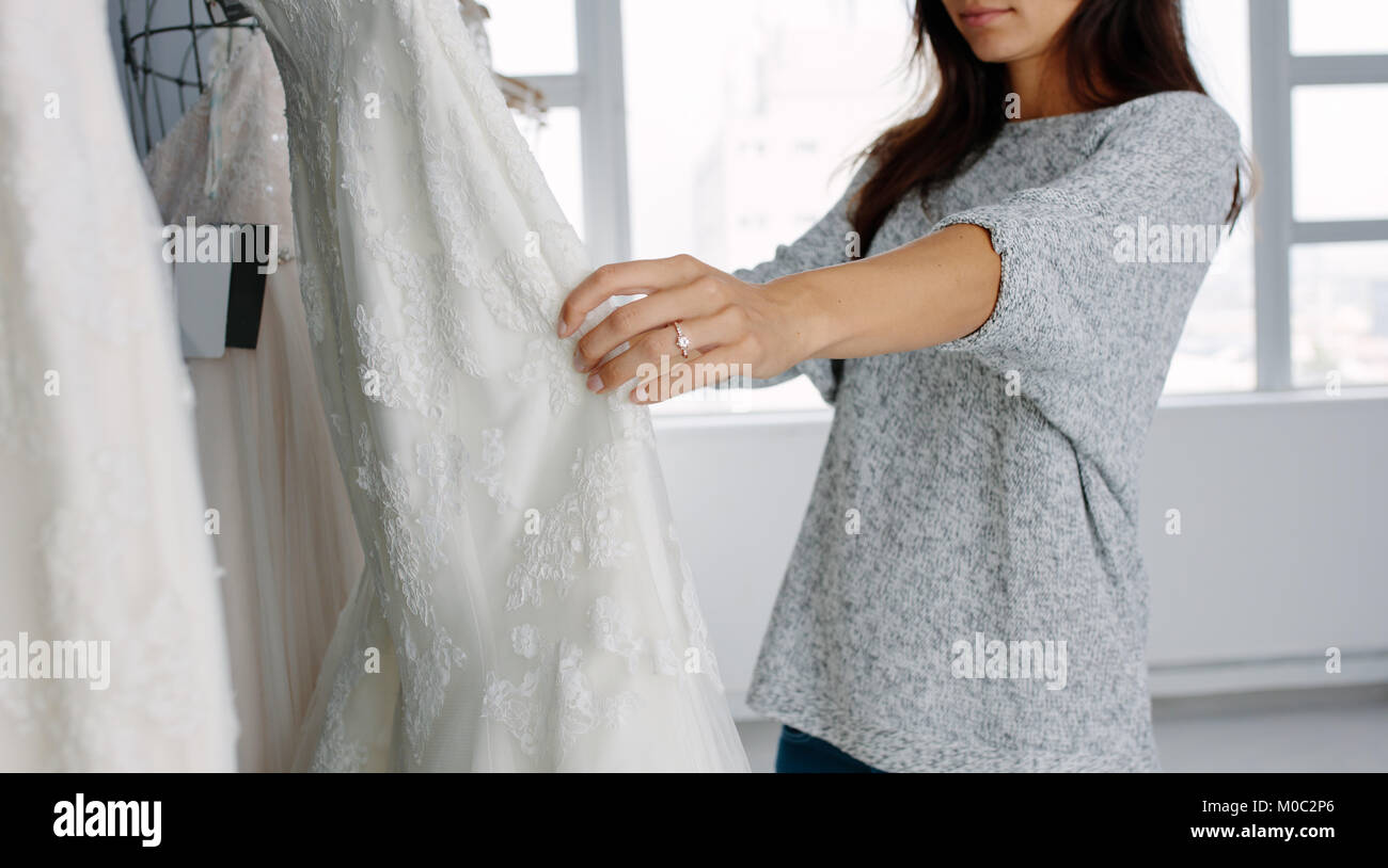 Giovane donna guardando abito nuziale sul display nella boutique. Concentrarsi sulle mani femminili la scelta di un abito da sposa dal display ad un matrimonio negozio di moda. Foto Stock
