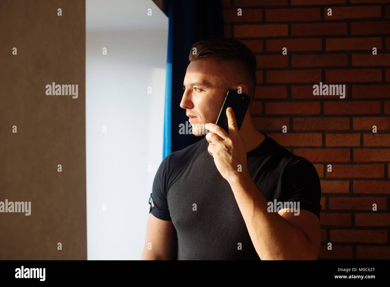 Uomo che parla al telefono in casa vicino alla finestra Foto Stock