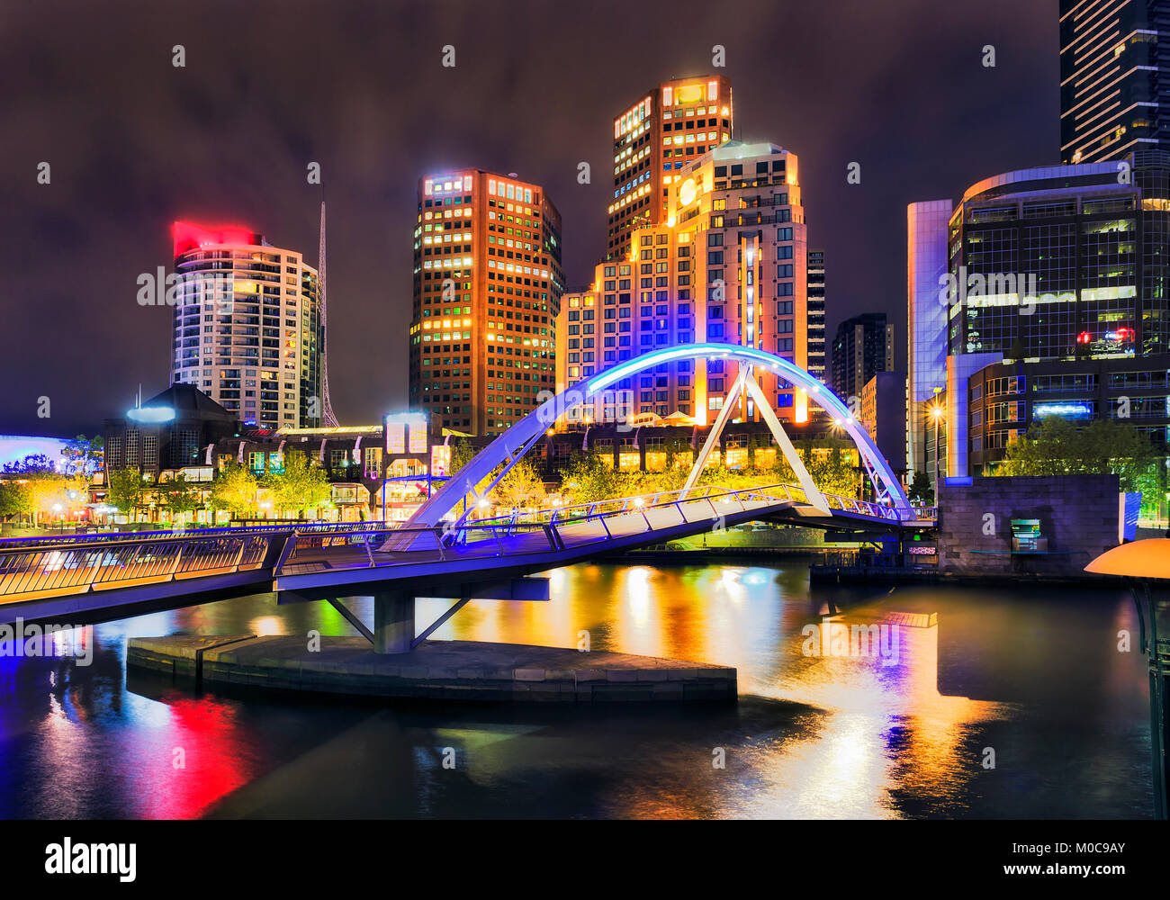 Di notte la città di Melbourne CBD landmark sulla sponda sud del fiume Yarra intorno al piede dello scuotipaglia con ponte luminoso luci urbane reflectign ancora in acque. Foto Stock
