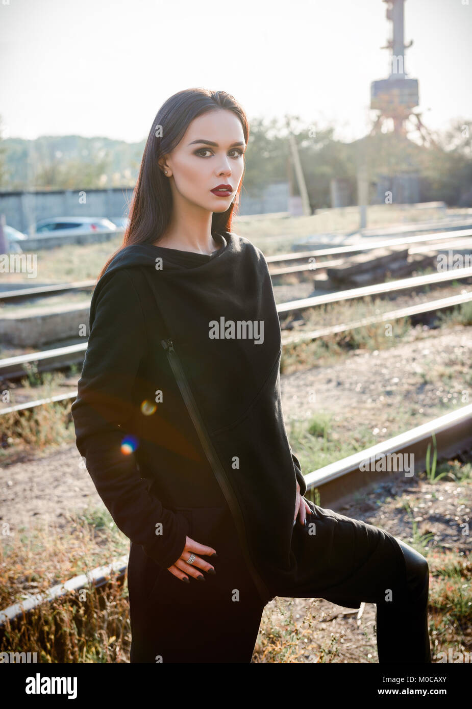 Moda shot: ritratto della bella ragazza rock (modello informale) in tunica e pantaloni in piedi alla ferrovia (zona industriale) Foto Stock