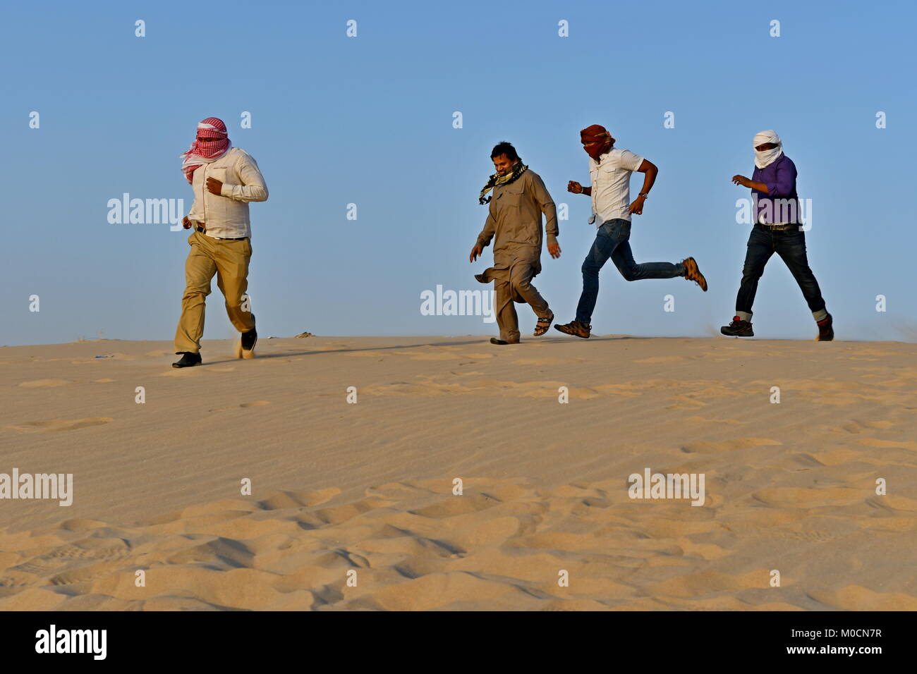 Gli uomini nel deserto di sabbia giocando ed appendere fuori con i telefoni cellulari e rendendo selfies Foto Stock