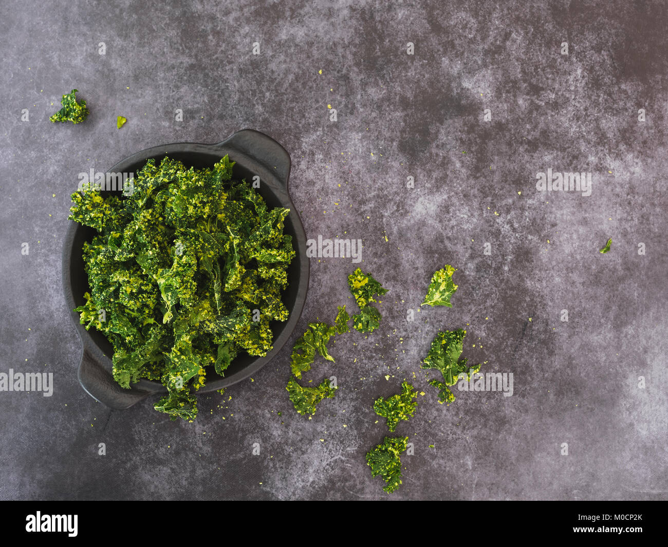 In casa cotto kale chip rivestito con olio di oliva e spolverate con sale marino su una piastra. Vista superiore, sfondo scuro, spazio vuoto Foto Stock