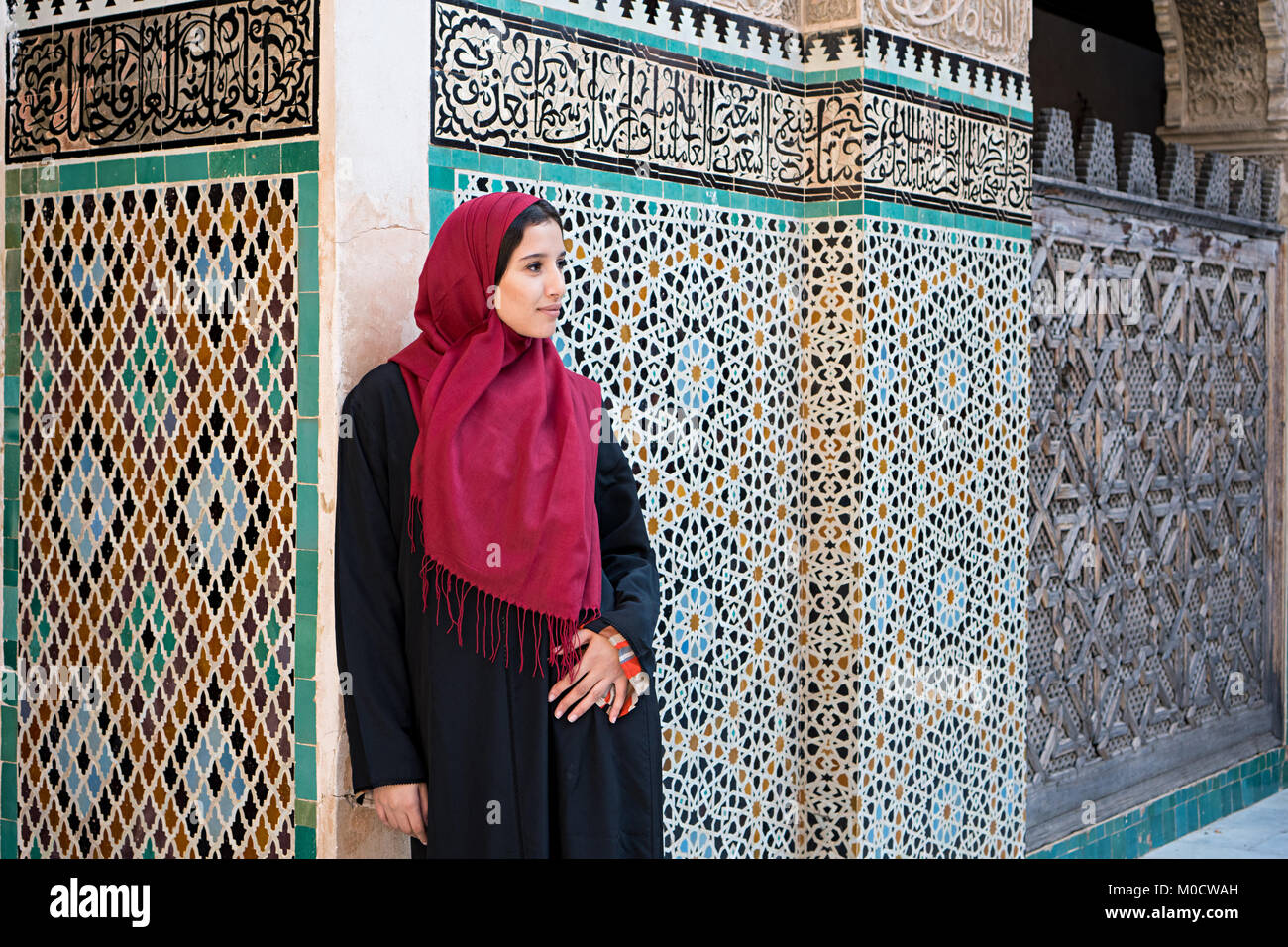 La donna araba in abbigliamento tradizionale con red hijab davanti al muro con testo dal Corano Foto Stock