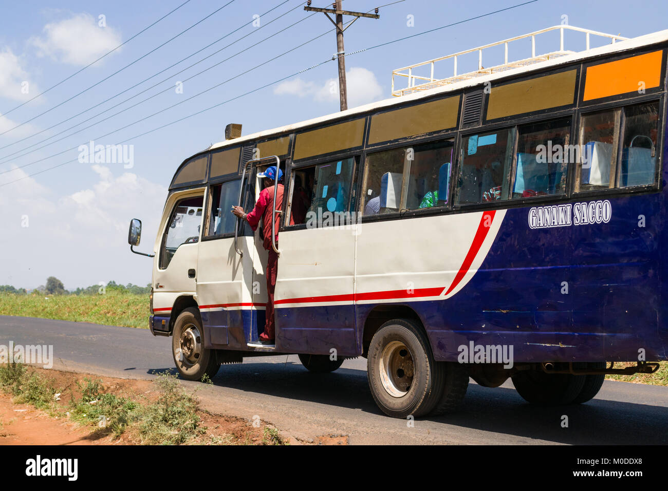 Un bus la guida su una strada con il conduttore in piedi la porta di attesa per i passeggeri, Nairobi, Kenia Foto Stock