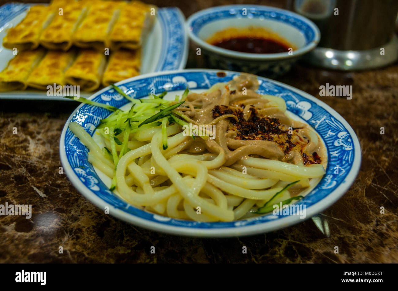 Una ciotola di spaghetti freddi con salsa di sesamo (majiang liangpi). In background Xi'an stile Gnocchetti fritti (guotie). In un ristorante del Quar musulmano Foto Stock