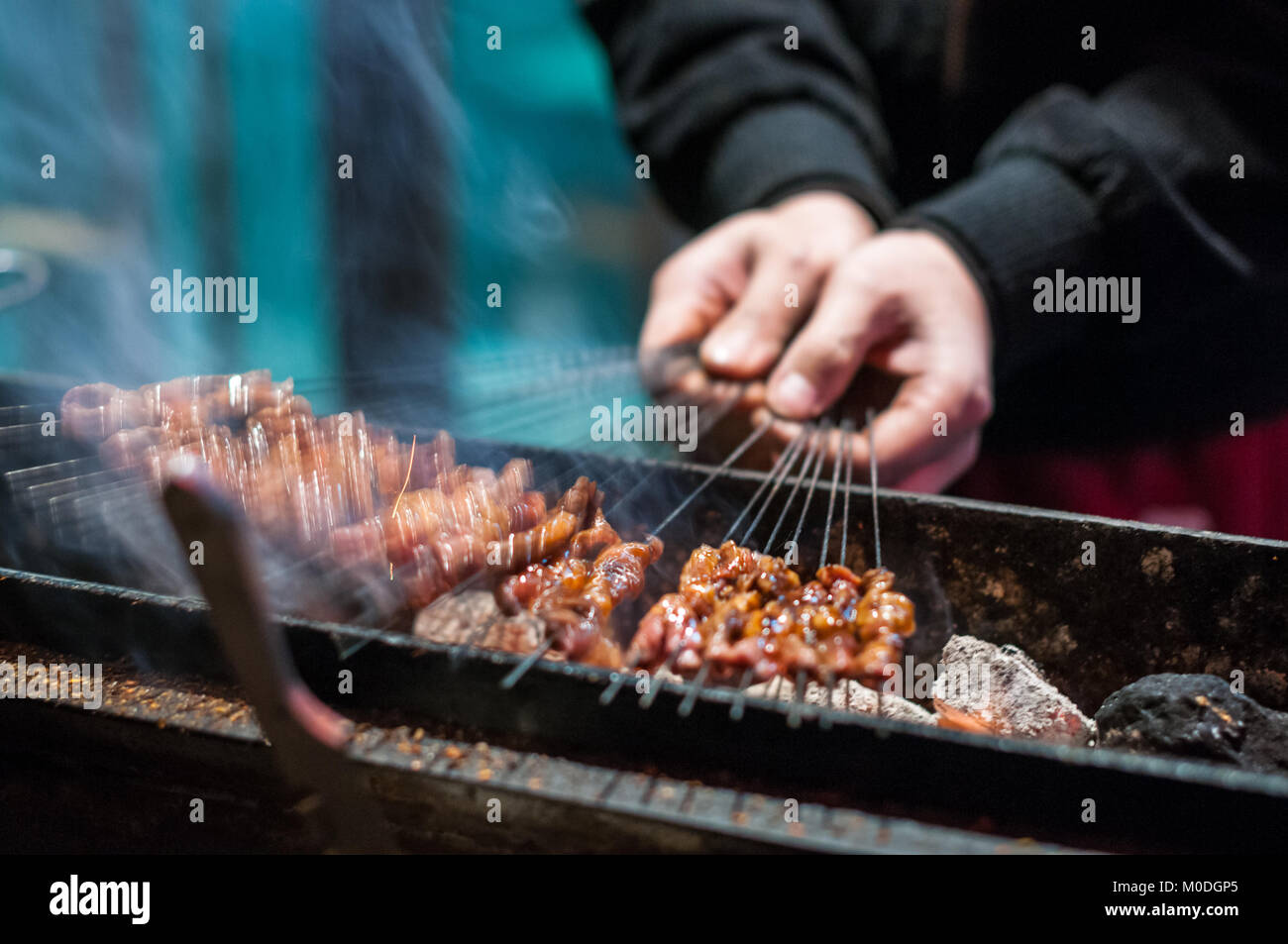 Un uomo alla brace piccoli spiedini di carne su spiedini di metallo tra i vicoli del quartiere musulmano di Xi'an, Cina. Uno di una serie di tre. Come ha visitato o Foto Stock