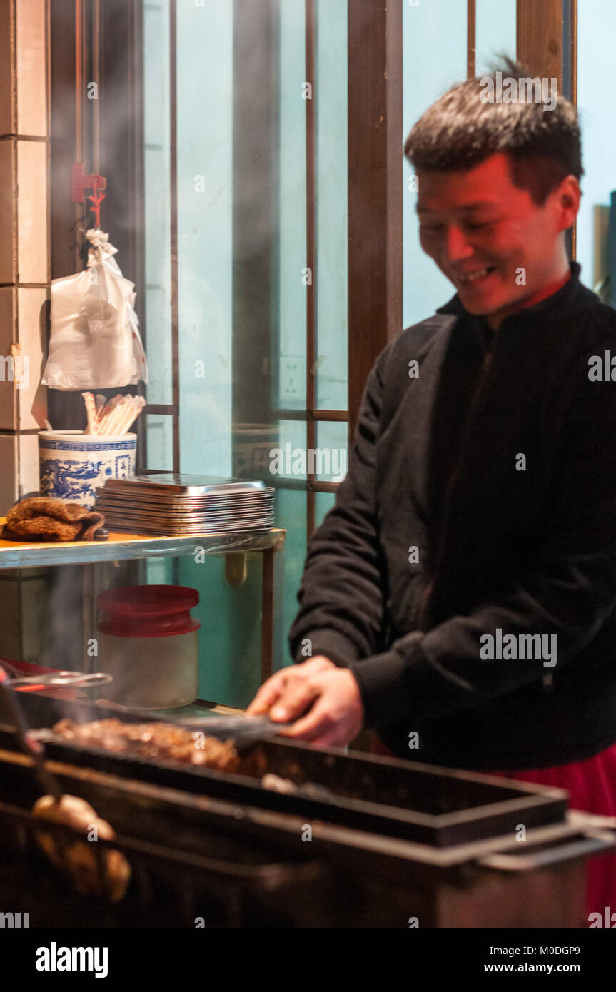 Un uomo alla brace piccoli spiedini di carne su spiedini di metallo tra i vicoli del quartiere musulmano di Xi'an, Cina. Uno di una serie di tre. Come ha visitato o Foto Stock