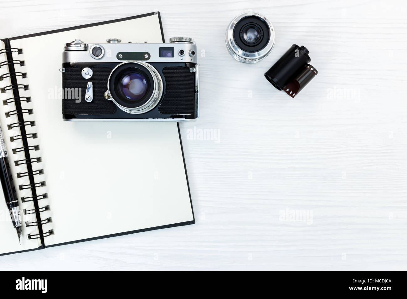 Foto vecchia telecamera, obiettivo rotolo pellicola, notebook e penna bianca su sfondo di legno vista piana Foto Stock