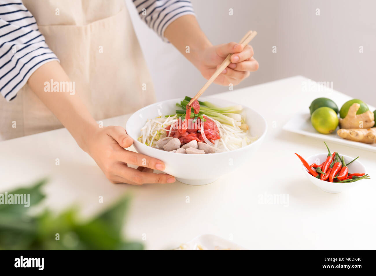 Femmina cuoco preparare la tradizionale zuppa vietnamita Pho bo con erbe aromatiche, carne e riso tagliatelle Foto Stock