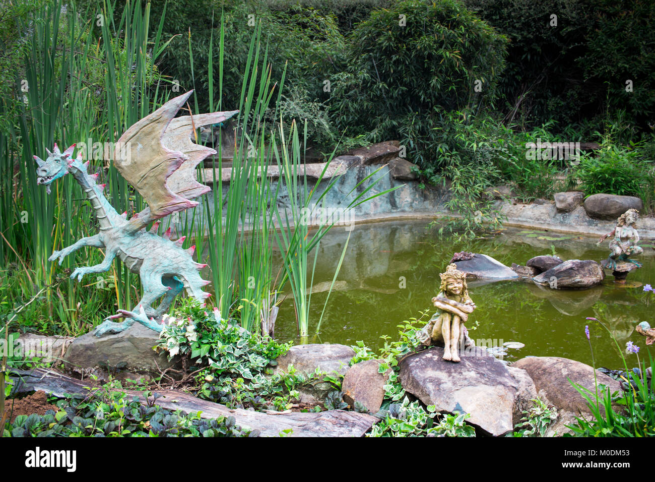 Drago decorativo e statue di fata seduta sul bordo del laghetto in giardino Foto Stock