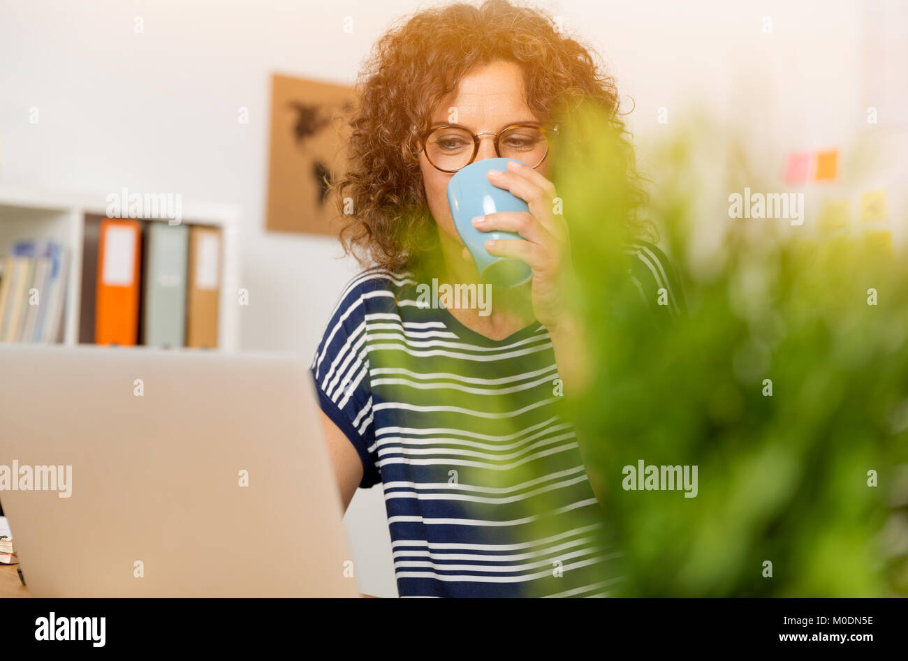 Donna di mezza età bere un caffè caldo in ufficio Foto Stock