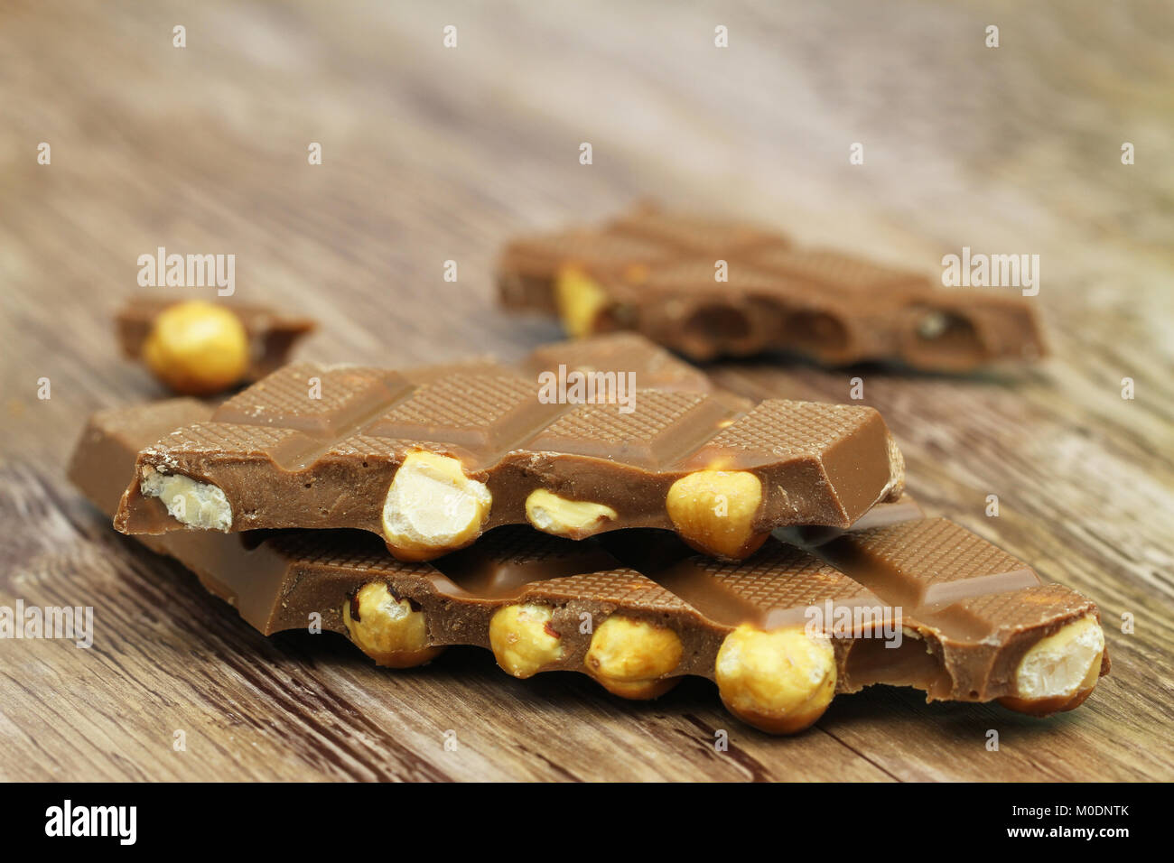 Pezzi di cioccolato al latte con nocciole intere su una superficie di legno Foto Stock