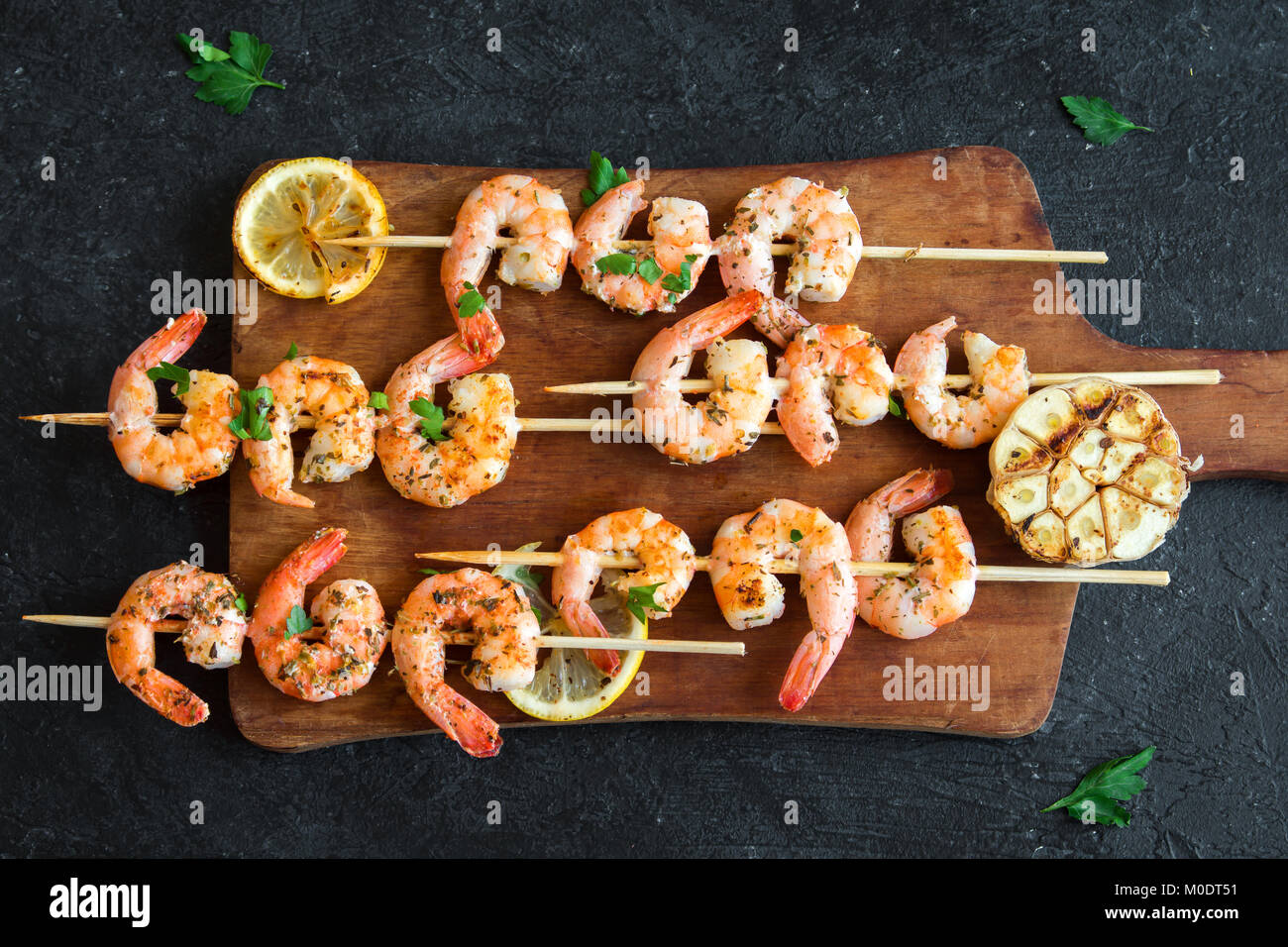 Grigliata di gamberi spiedini. Frutti di mare, shelfish. Gamberi spiedini con erbe aromatiche, aglio e limone su pietra nera di sfondo, copia dello spazio. Gamberi b Foto Stock