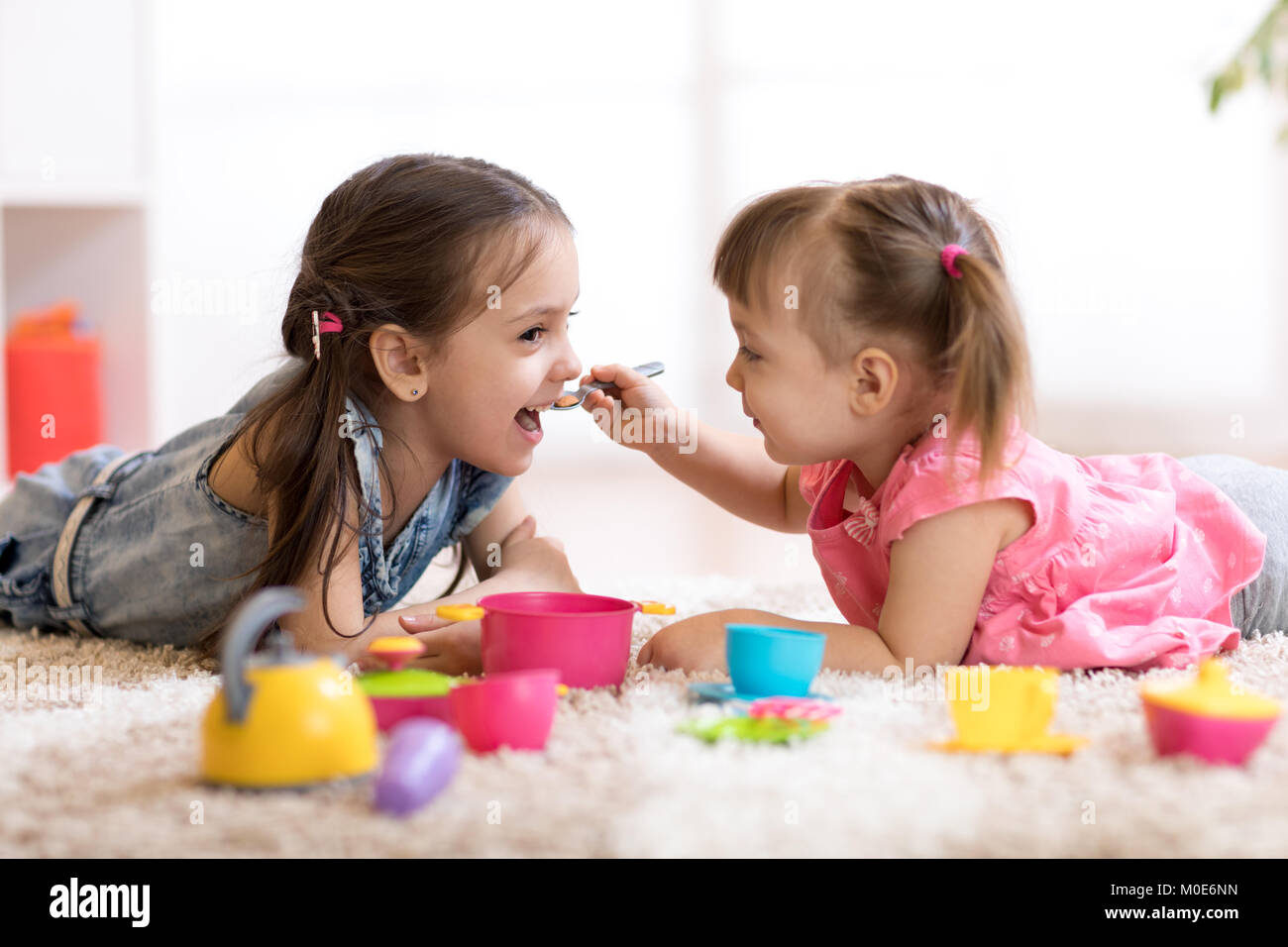 Carino piccolo i bambini giocando con stoviglie giocattoli sdraiati sul pavimento a casa Foto Stock