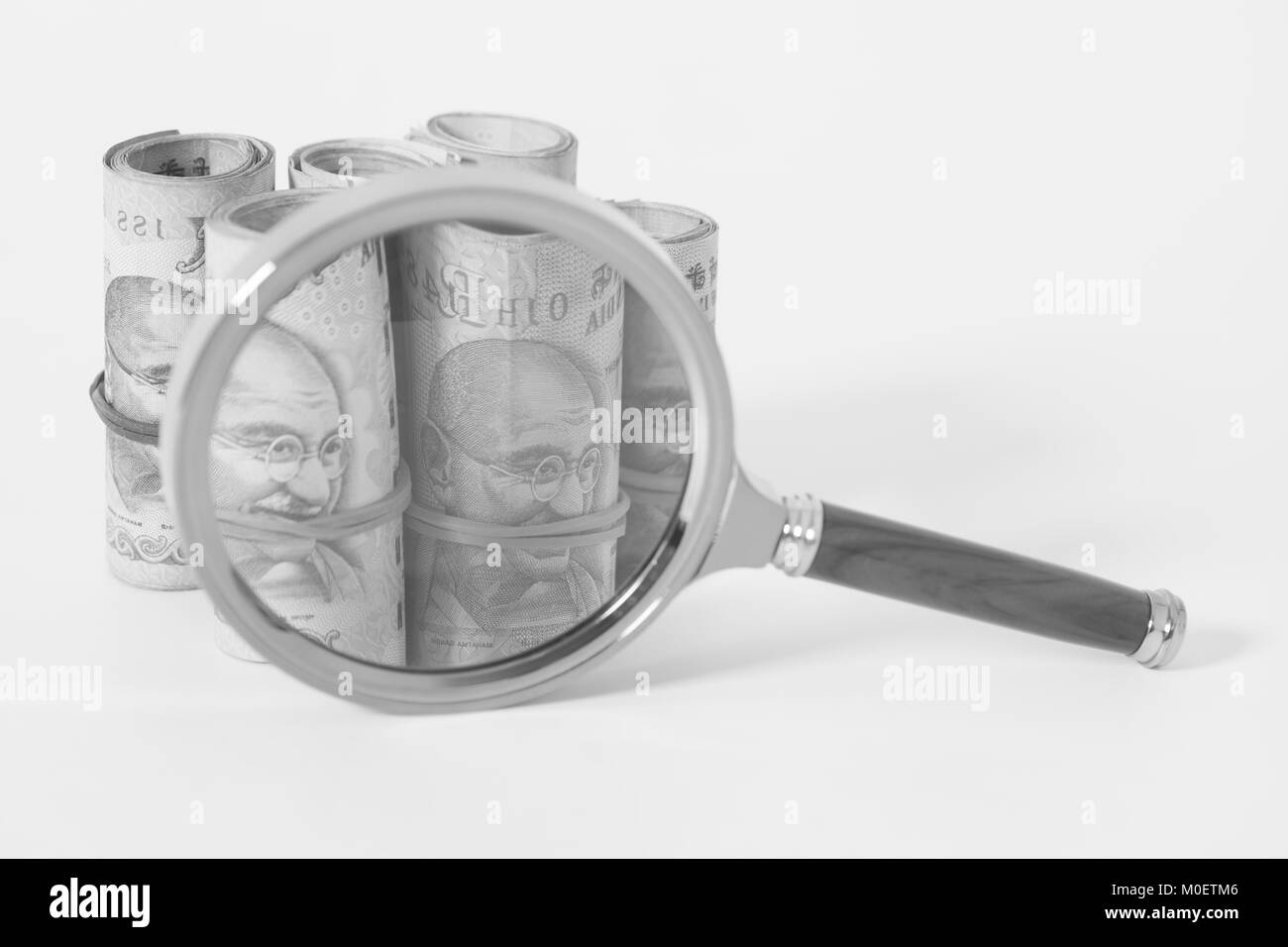 Rotoli di valuta indiana Rupee note con lente di ingrandimento isolato su bianco Foto Stock