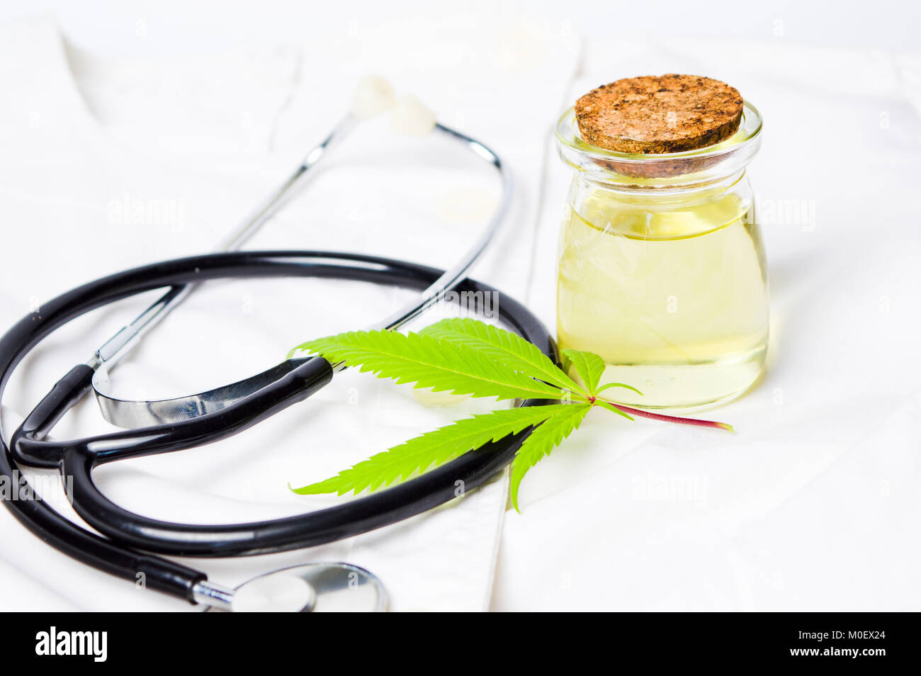 Foglia di marijuana, olio e uno stetoscopio sulla tuta medica Foto Stock