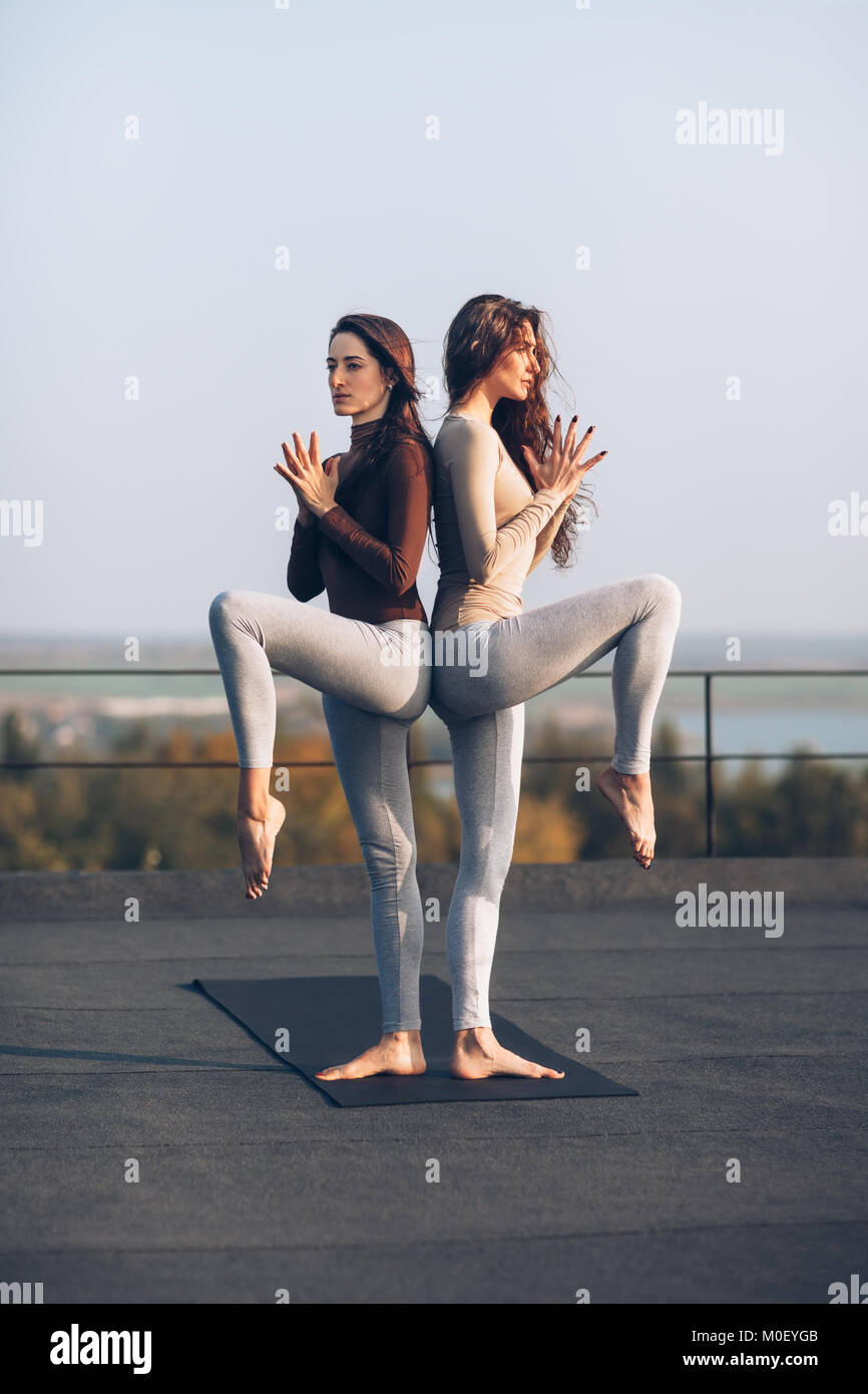 Ragazze in coppia permanente yoga posa di schiena sul tetto all'aperto. Due belle donne sono concentrati sul fare esercizio permanente, mentre con sollevamento Foto Stock