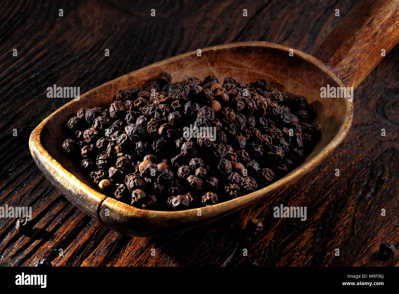 Pepe nero in cucchiaio di legno sul tavolo di legno Foto Stock