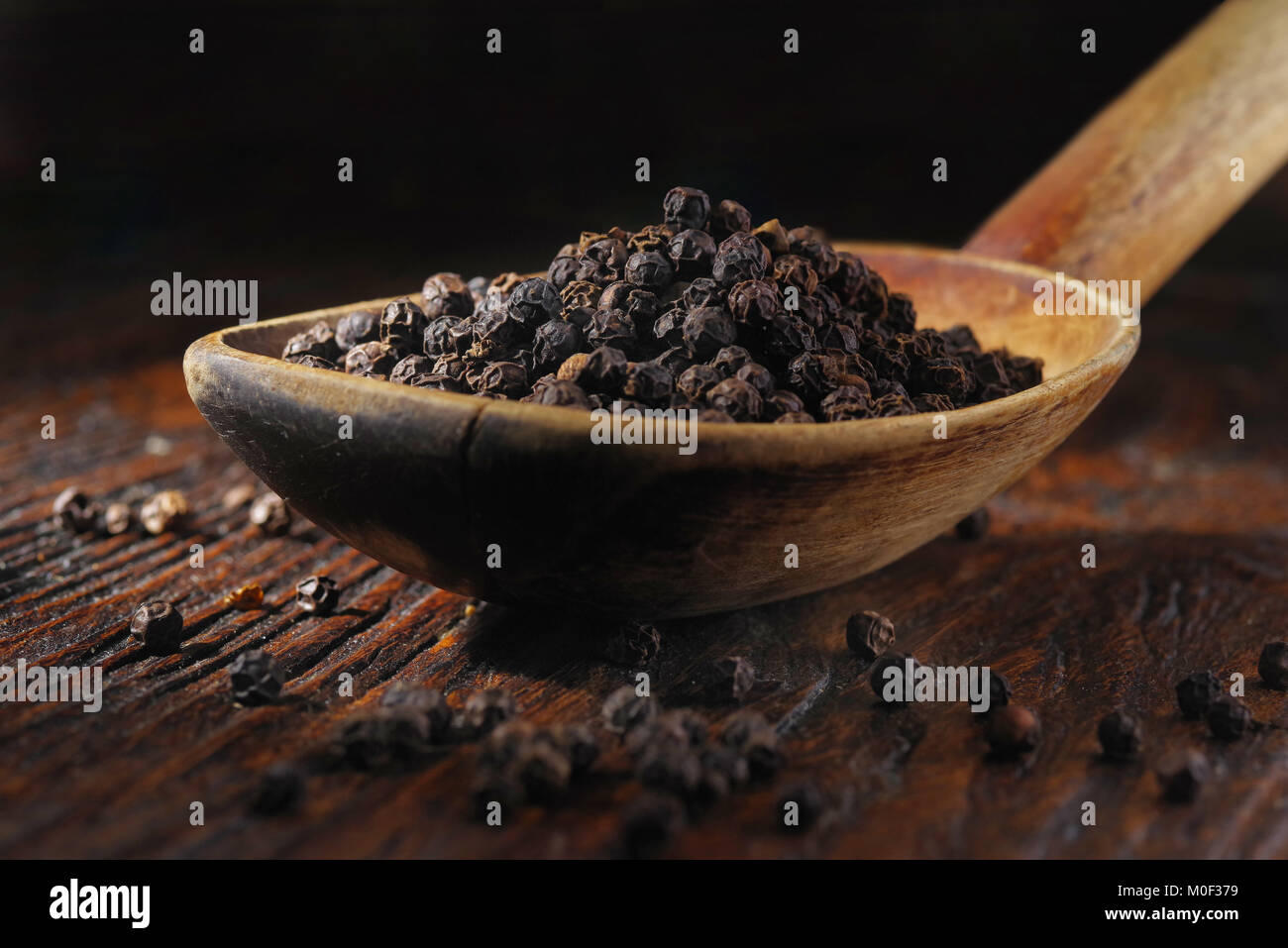 Pepe nero in cucchiaio di legno sul tavolo di legno Foto Stock