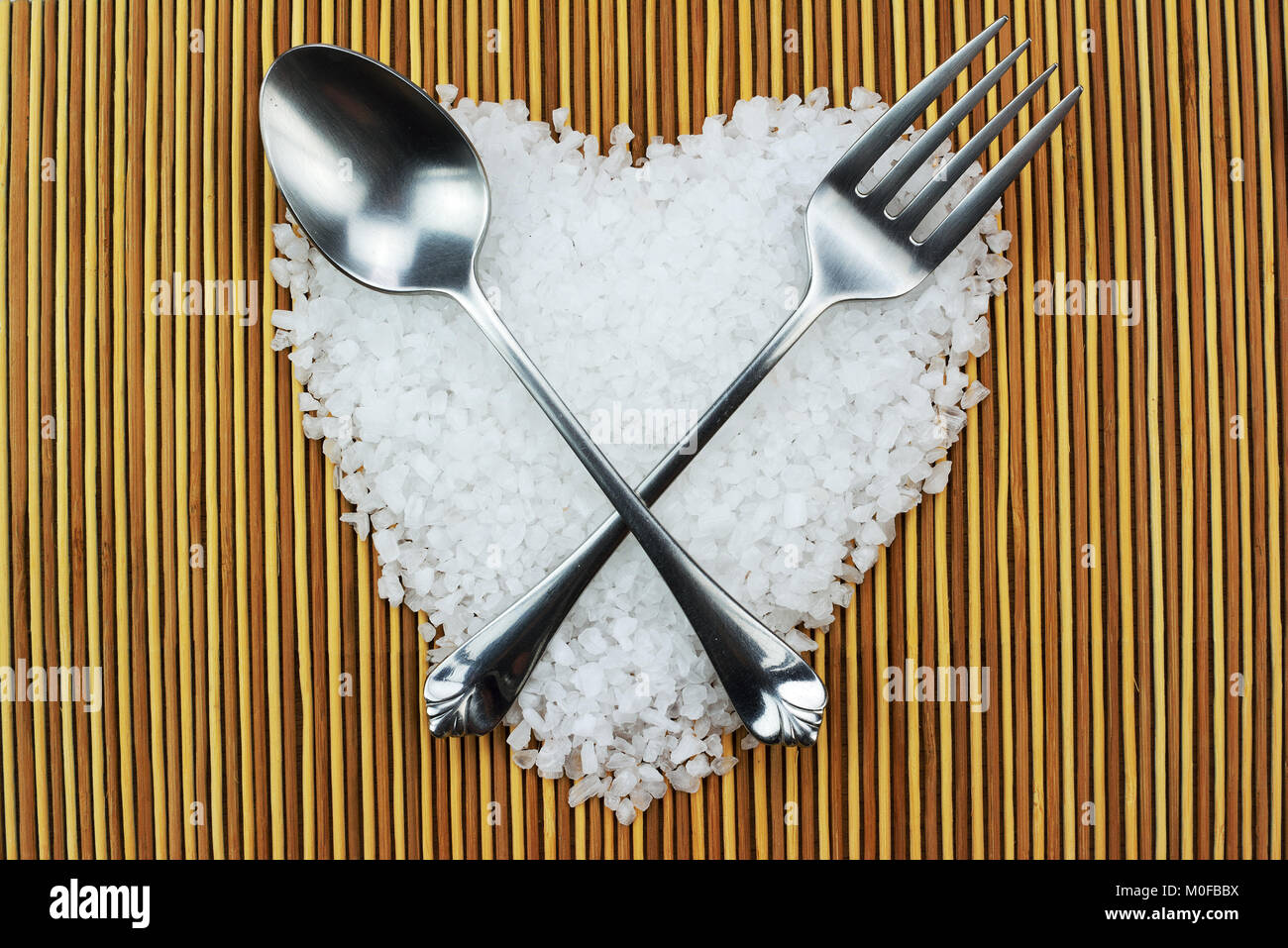 Il sale di mare a forma di cuore con argento cucchiaio e forchetta su sfondo tappetini Foto Stock