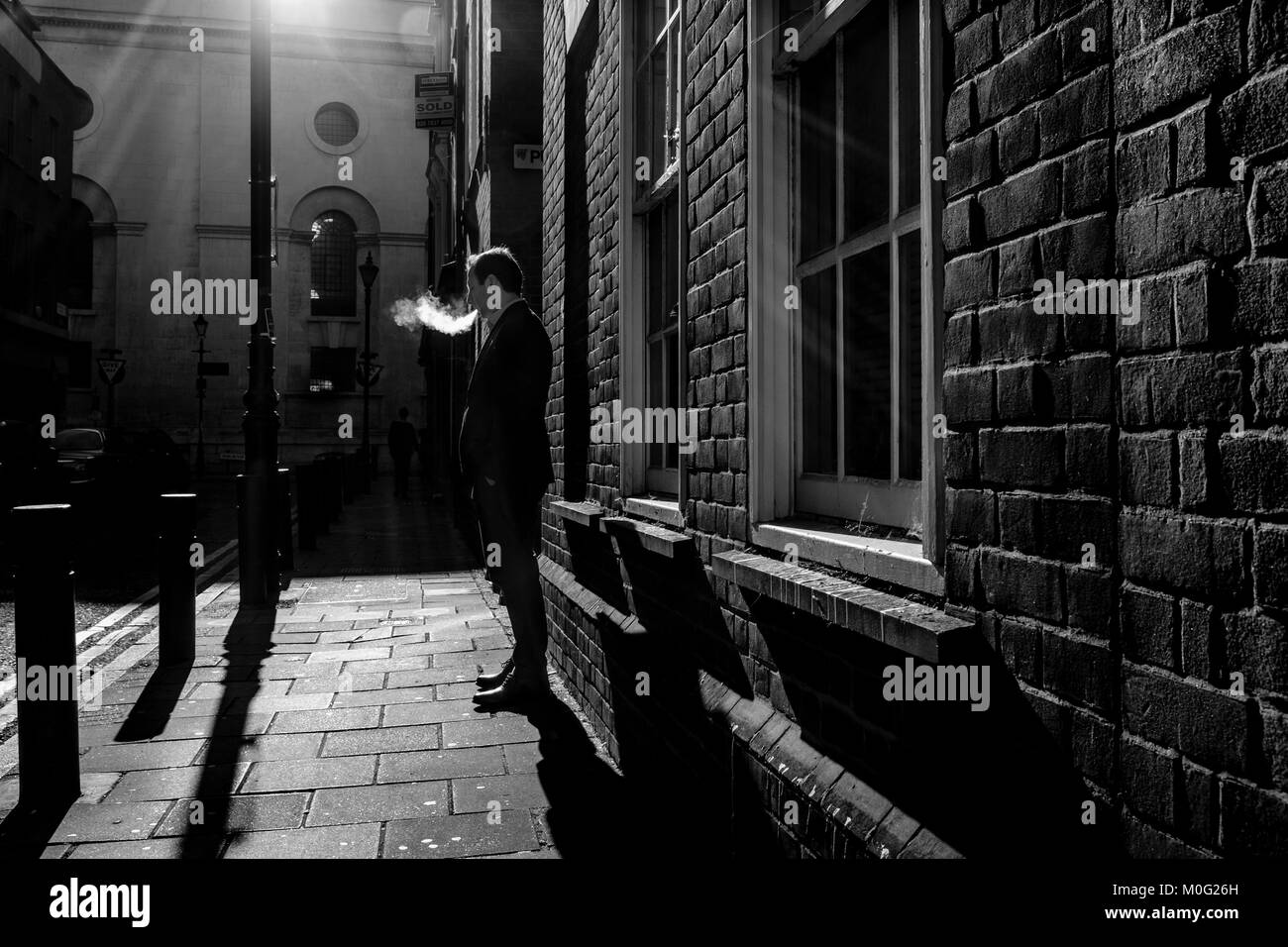 Fotografia di strada in bianco e nero a Londra: Uomo che fuma in strada. Foto Stock