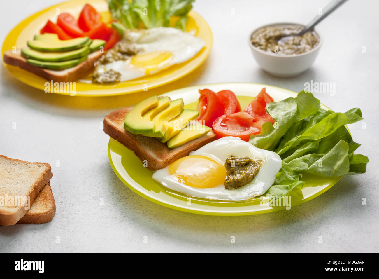 Dieta sana prima colazione. toast con fette di avocado, Uovo fritto, pomodori, crescione, pesto su una piastra su un sfondo di calcestruzzo Foto Stock