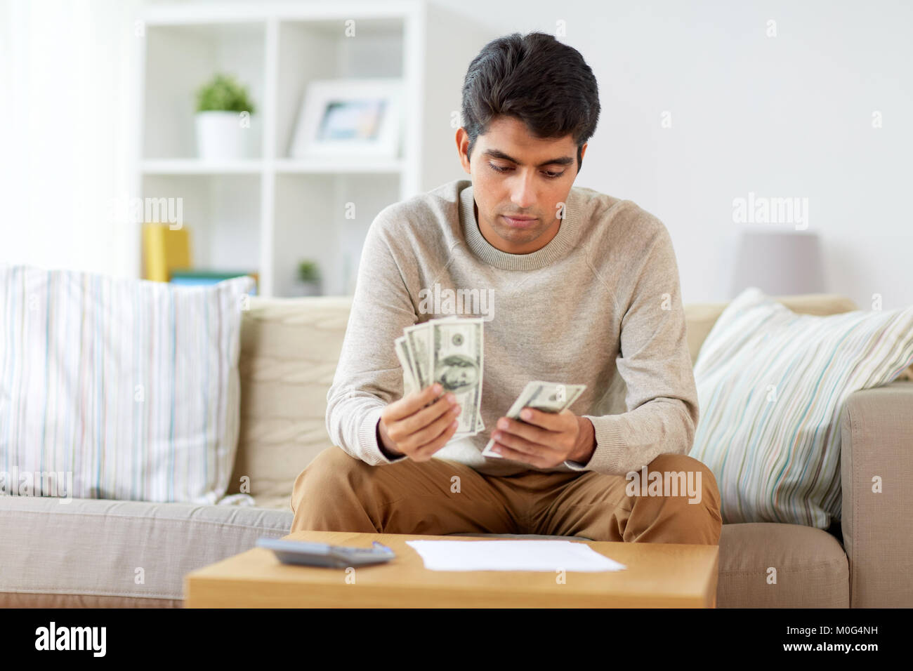 L'uomo con la calcolatrice conteggiare denaro a casa Foto Stock