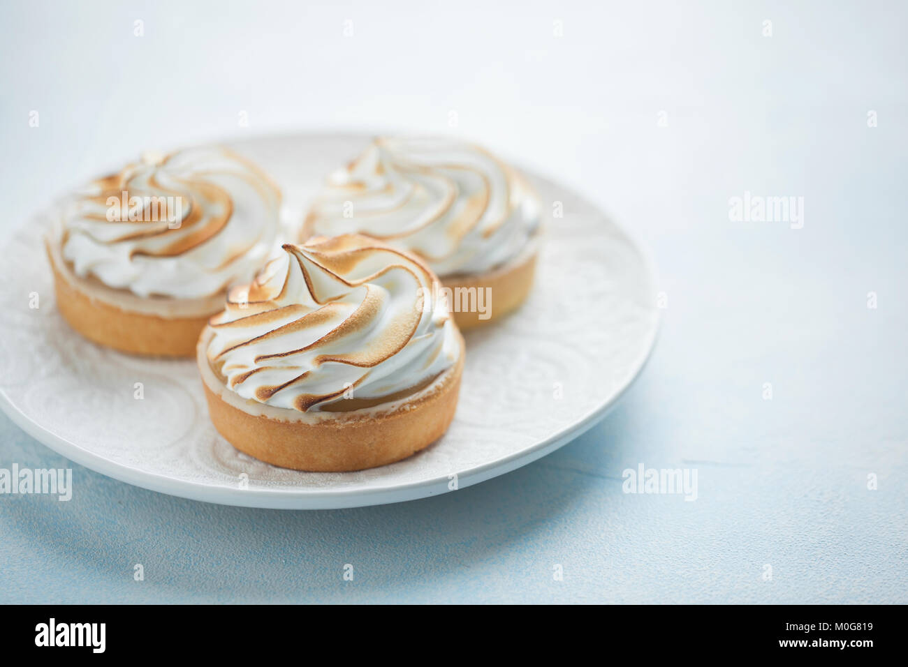 Deliziosi pasticcini al limone con meringa su un bianco piastra vintage. Dolce trattare su un fondo azzurro. Foto Stock