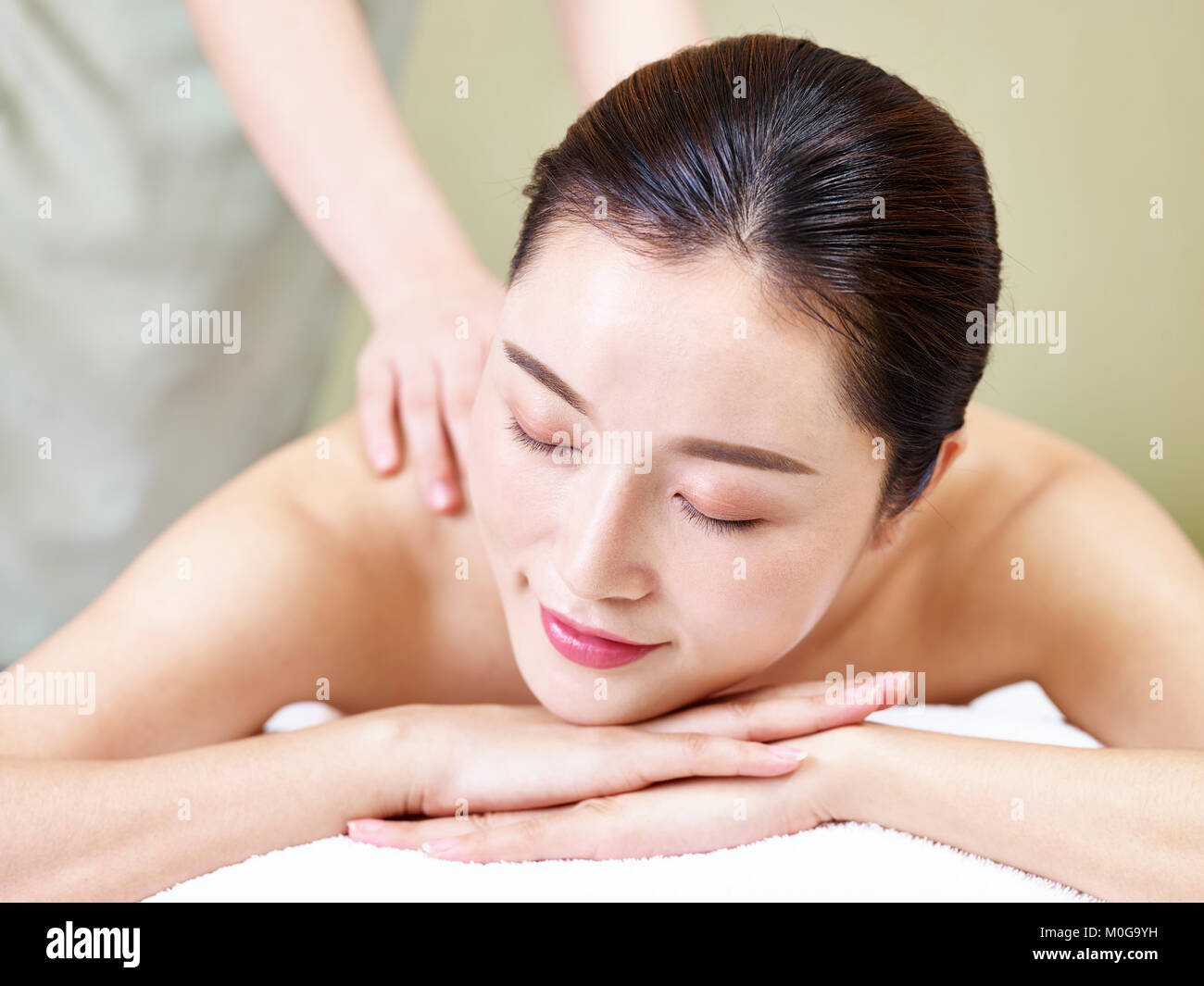 Close-up del volto di una giovane e bella donna asiatica che giace sulla parte anteriore sul letto ricevente in massaggio spa salone. Foto Stock