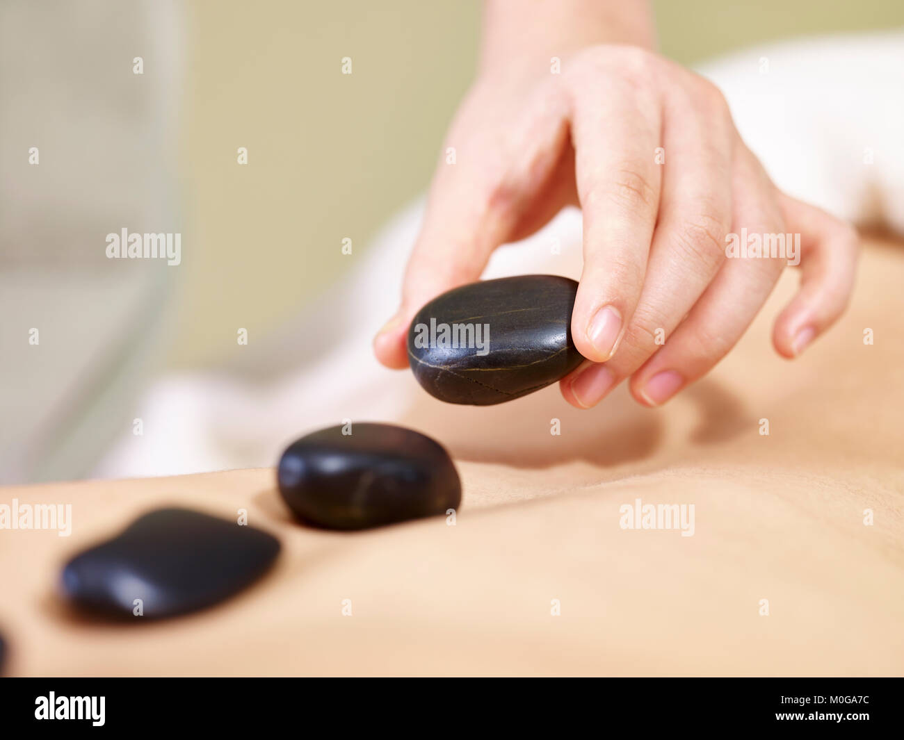 Close-up di mani di un massaggiatore porre pietra su retro del cliente per eseguire un massaggio con pietre calde. Foto Stock