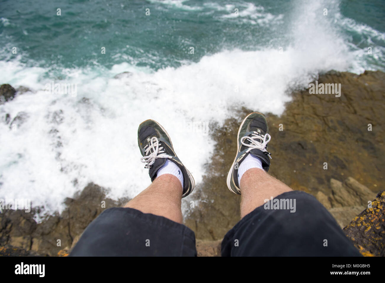Gambe essendo dangled sulla cima di una scogliera a Storm Bay in Kiama, Nuovo Galles del Sud, Australia Foto Stock