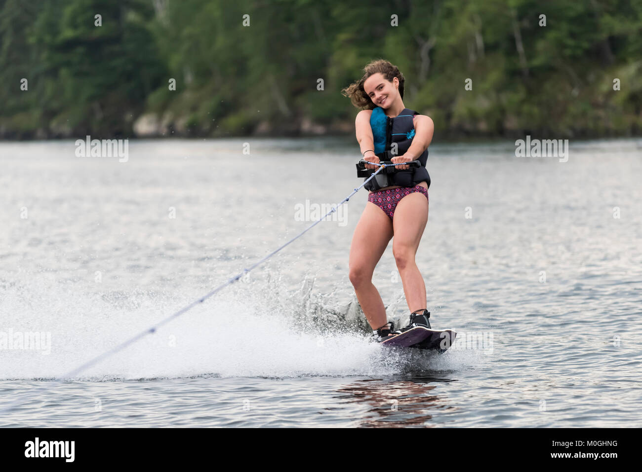 Una ragazza adolescente wakeboarding dietro una barca sul lago; il lago dei boschi, Ontario, Canada Foto Stock