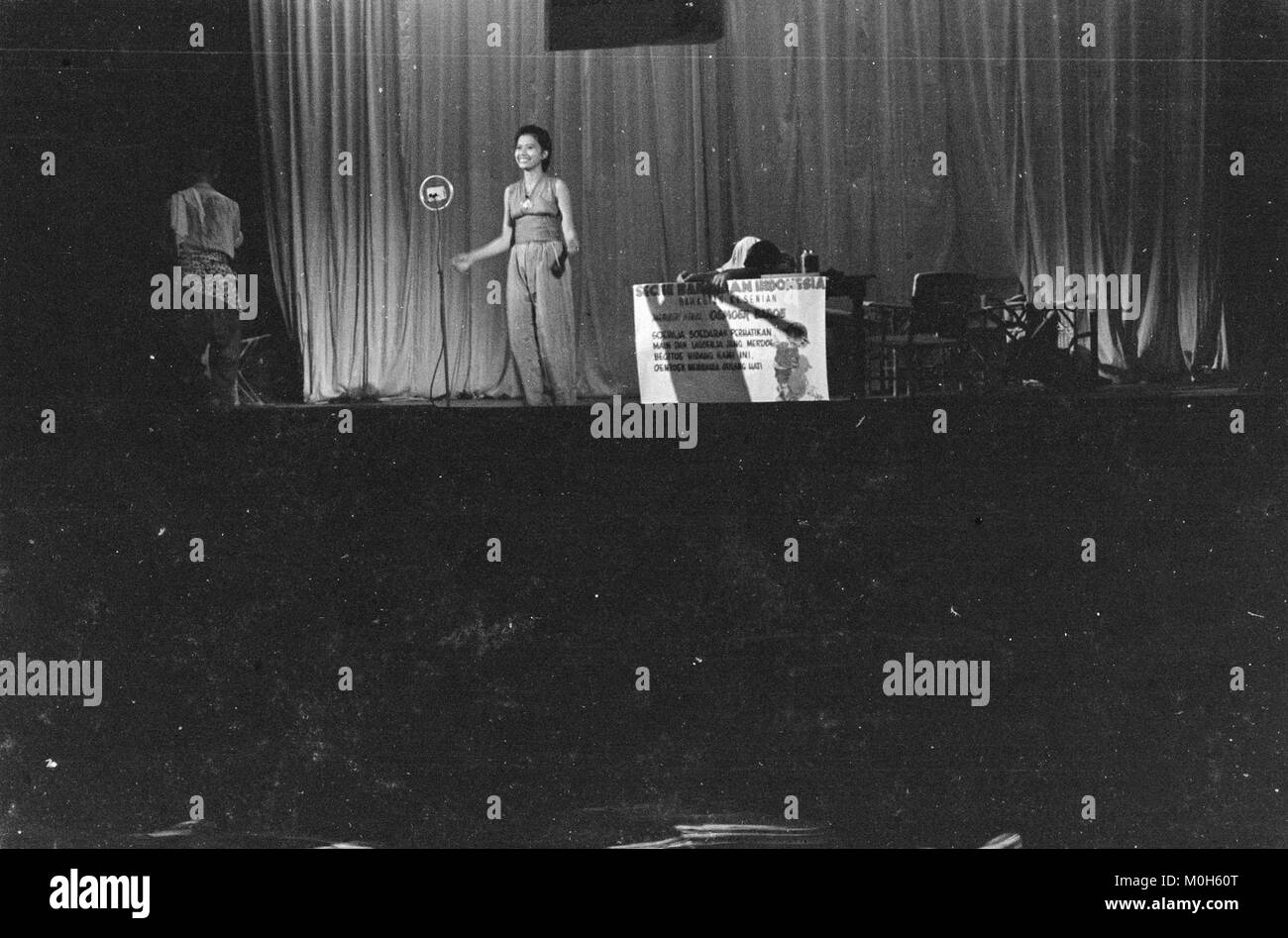 Fotografia di uno spettacolo di cabaret che mostra un uomo seduto a un tavolo e una donna in piedi nelle vicinanze, catturando una scena teatrale con linguaggio espressivo del corpo. Foto Stock