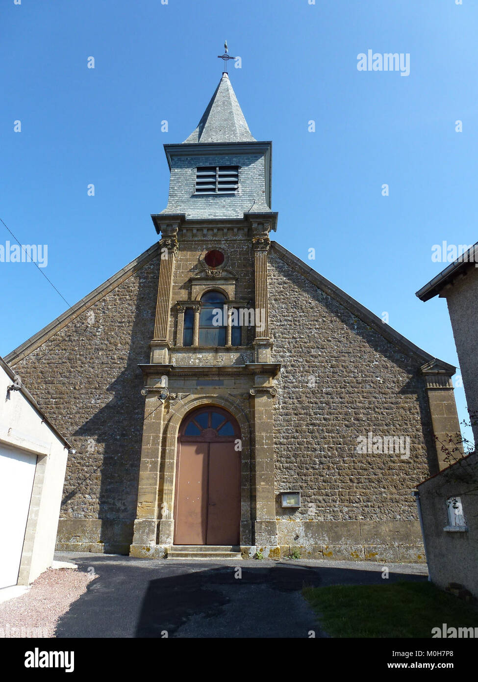 Questa fotografia mostra la facciata della chiesa a Bouvellemont, un comune della regione francese delle Ardenne. La struttura presenta una tradizionale architettura rurale francese, caratterizzata da muratura in pietra, un tetto a timpano e un campanile centrale. Foto Stock