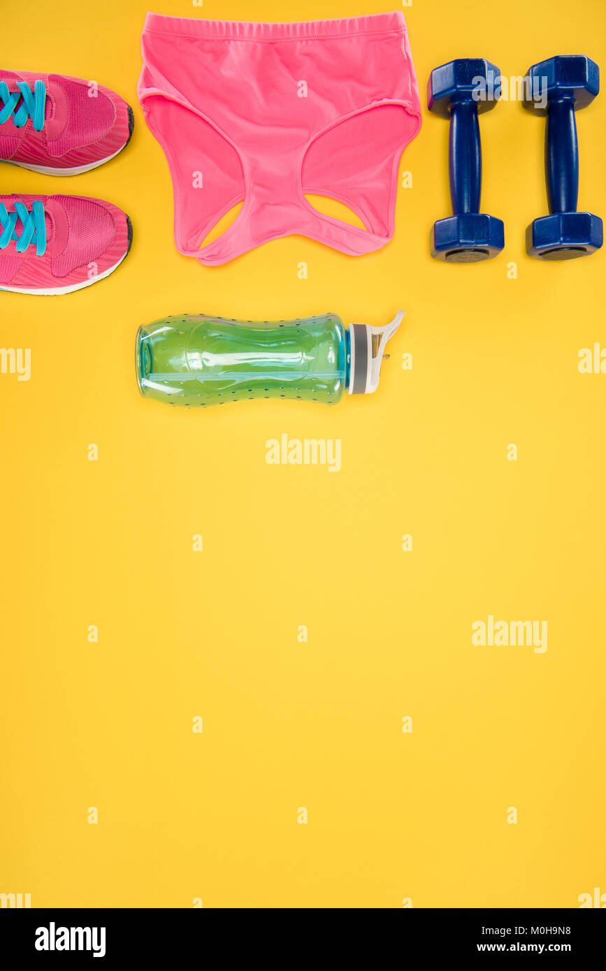 Attrezzature sportive con scarpe, manubri, sport top e una bottiglia d'acqua isolato su giallo Foto Stock