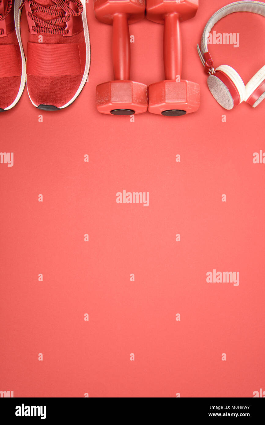 Attrezzature sportive con le scarpe, i pesi e le cuffie isolato su rosso Foto Stock