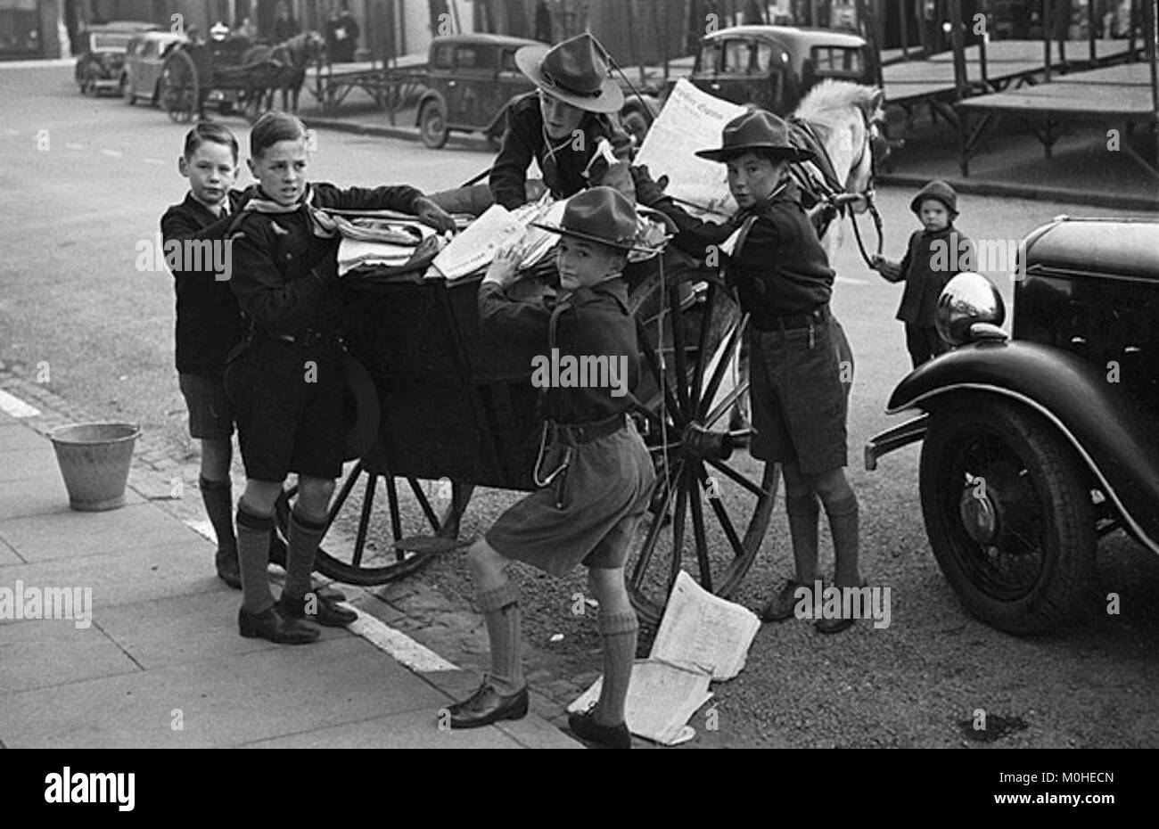La fotografia mostra i giovani volontari della squadra di Newtown Scout che raccolgono carta di scarto in contenitori e borse all'aperto, illustrando un'iniziativa di riciclaggio della comunità. I partecipanti indossano parti uniformi da scout e operano in uno spazio pubblico come una strada o un parco, riflettendo l'impegno civico e la gestione ambientale. Foto Stock