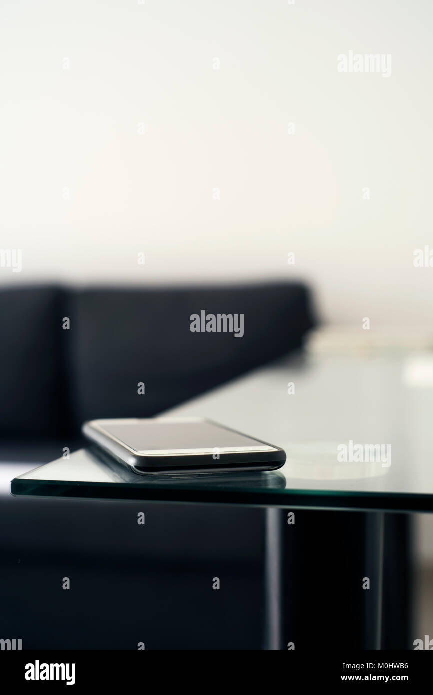 Primo piano di una smpartphone su un tavolo di vetro in un moderno soggiorno o una lobby, con uno spazio vuoto sulla parte superiore Foto Stock