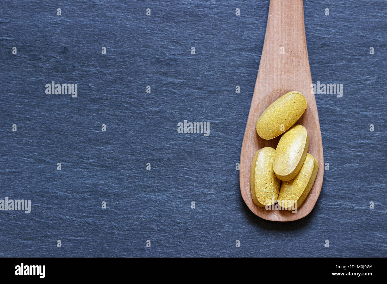 Supplemento pillole sul cucchiaio contro lo sfondo di ardesia Foto Stock