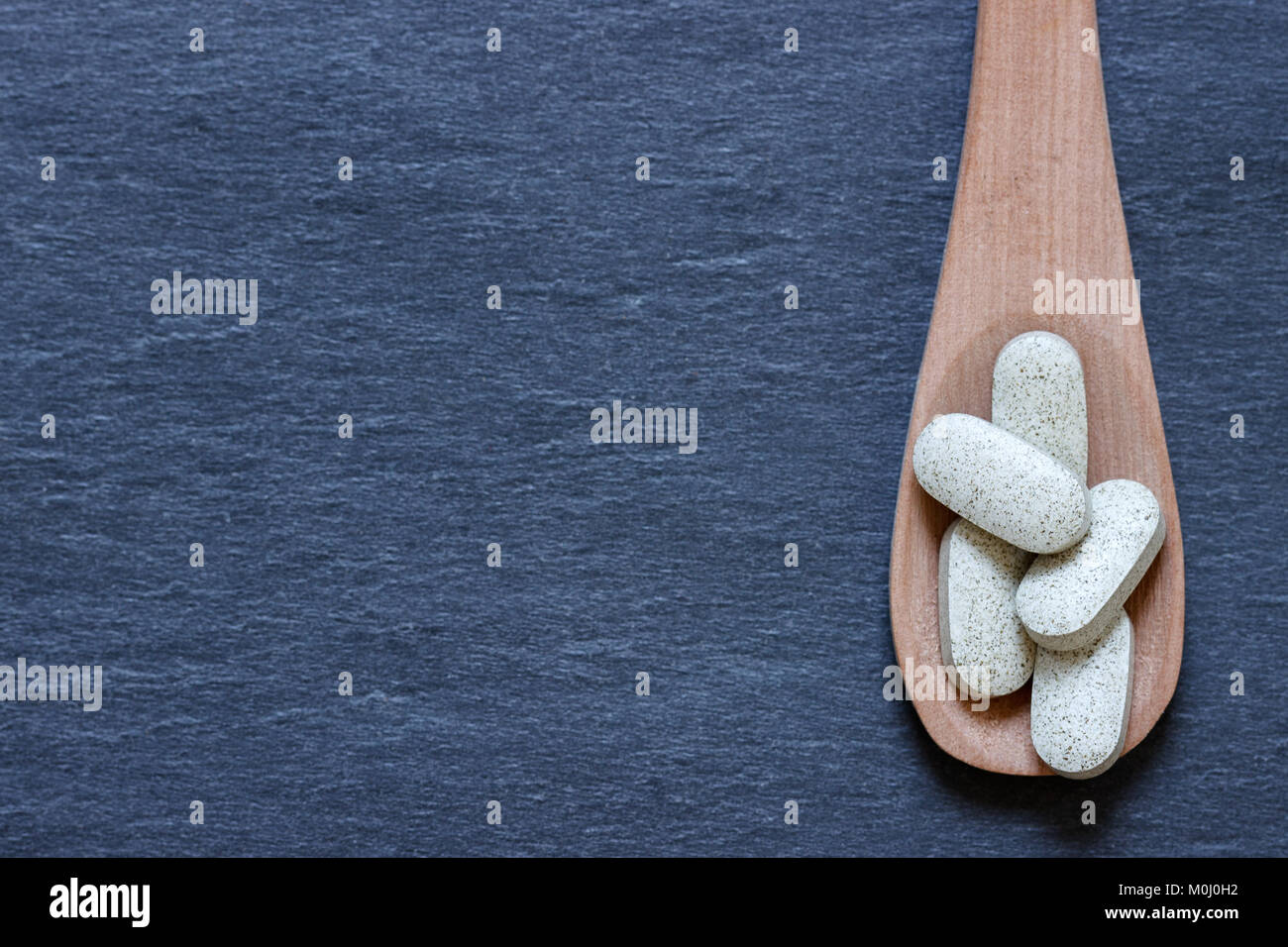 Supplemento pillole sul cucchiaio contro lo sfondo di ardesia Foto Stock